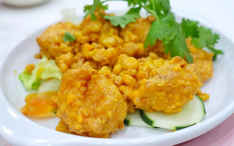 Salted egg yolk prawns with crunchy corn kernels on a plate garnished with cucumber and parsley